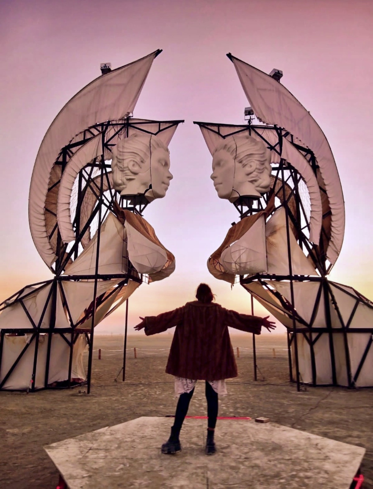 A seeker stands with arms open before the sphinxes at sunset